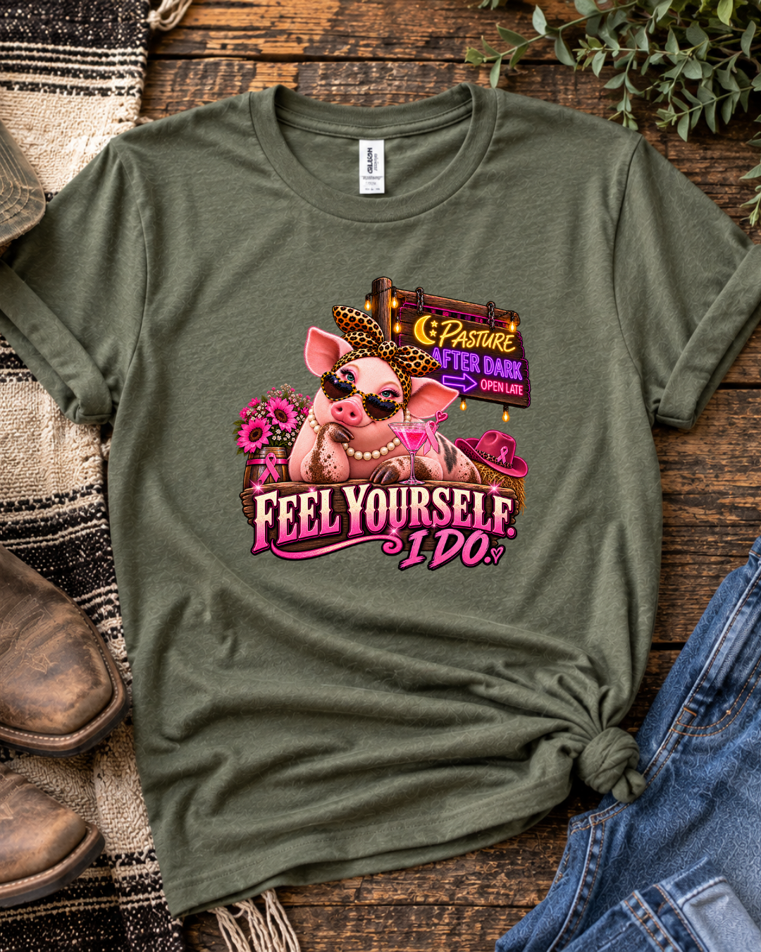 Olive green Feel Yourself I Do breast cancer awareness T-shirt with a pink farm-animal graphic, styled on a rustic wooden background.