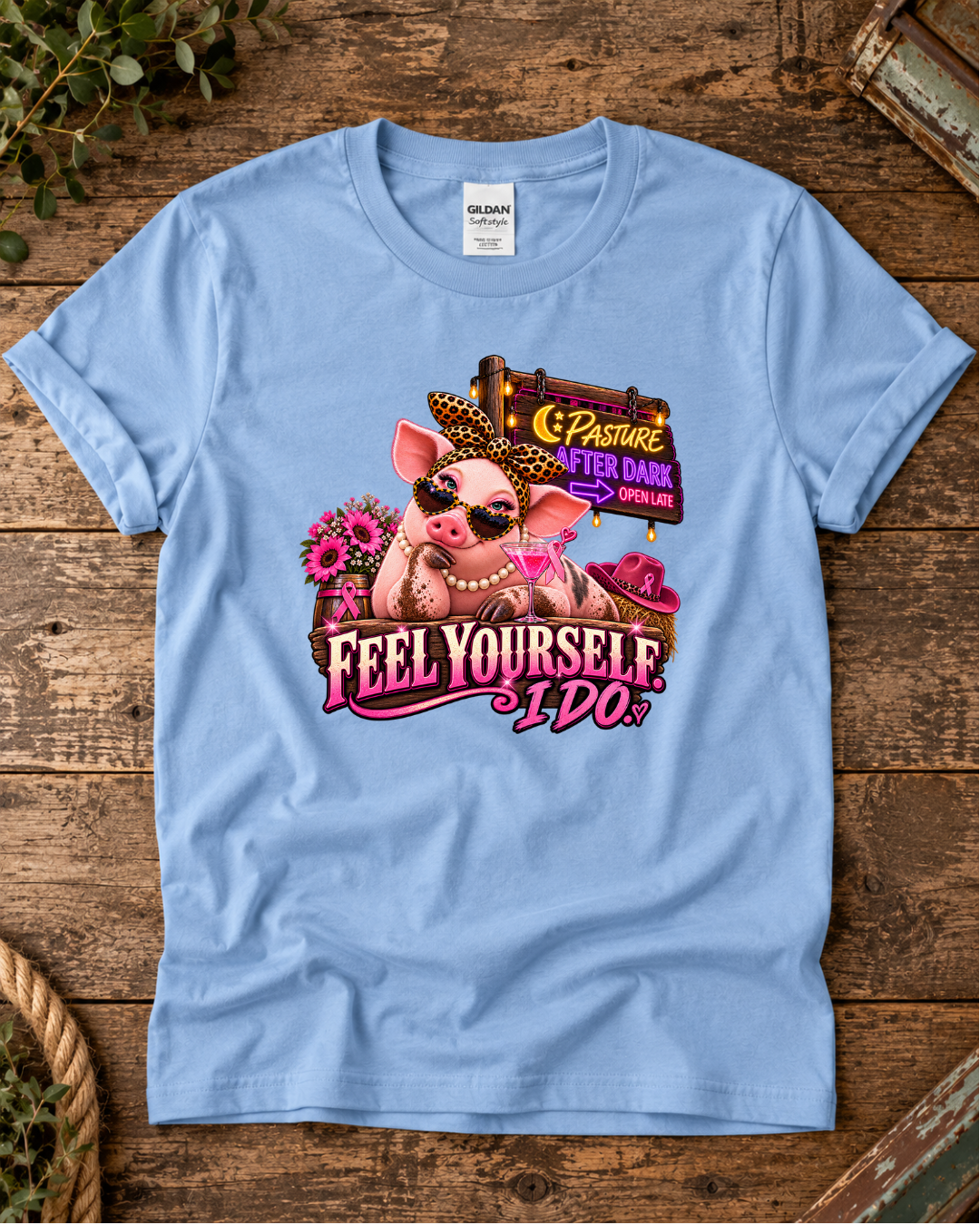 Light blue Feel Yourself I Do breast cancer awareness T-shirt with a colorful pink farm-animal graphic on a rustic wooden background.